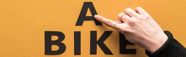 Обрезанный вид женщины, указывающей пальцем на надпись на велосипеде на оранжевом фоне — стоковое фото