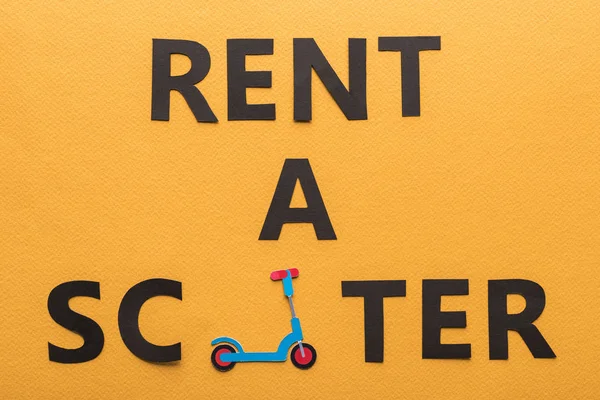 Top view of paper cut rent a scooter lettering on orange background — Stock Photo