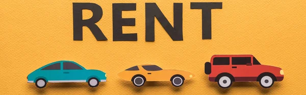 Draufsicht auf Papier geschnittene Autos und schwarzer Mietschriftzug auf orangefarbenem Hintergrund, Panoramaaufnahme — Stockfoto