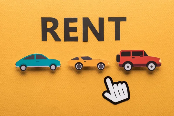 Top view of paper cut cars with pointing hand and black rent lettering on orange background — Stock Photo