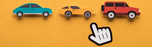 Vista superior de coches cortados en papel con la mano apuntando sobre fondo naranja, plano panorámico - foto de stock