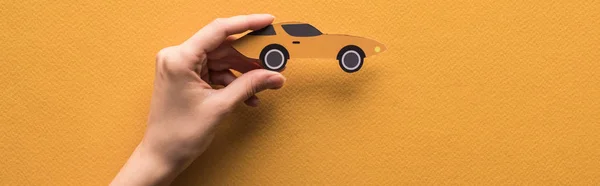 Cropped view of woman holding paper cut sports car on orange background, panoramic shot — Stock Photo