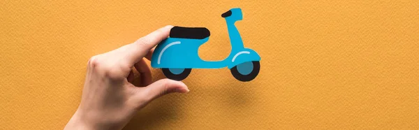 Cropped view of woman holding paper cut scooter on orange background, panoramic shot — Stock Photo