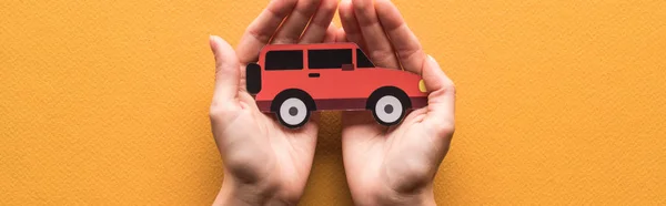 Partial view of woman holding paper cut car on orange background, panoramic shot — Stock Photo
