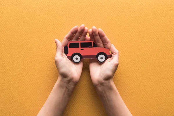 Teilansicht einer Frau mit papiergeschnittenem Auto auf orangefarbenem Hintergrund — Stockfoto