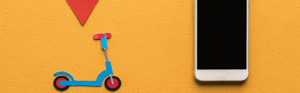 Top view of paper cut kick scooter, location mark near smartphone with blank screen on orange background, panoramic shot — Stock Photo