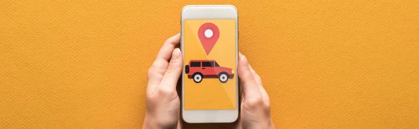 Vista recortada de la mujer que sostiene el teléfono inteligente con aplicación de alquiler de coches sobre fondo naranja, tiro panorámico - foto de stock