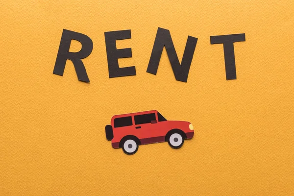 Draufsicht auf Papier geschnittenes Auto und schwarzer Rent-Schriftzug auf orangefarbenem Hintergrund mit Kopierraum — Stockfoto
