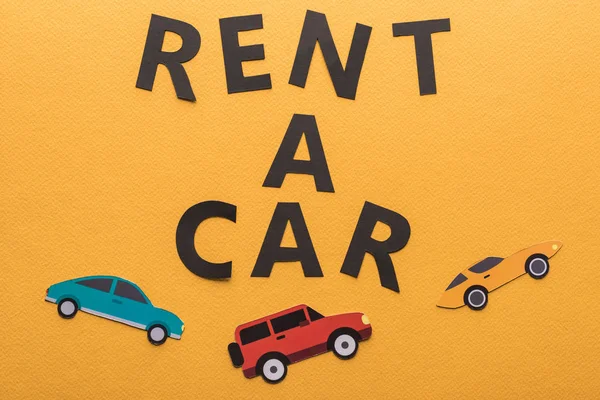 Draufsicht auf Papier geschnittene Fahrzeuge und schwarzer Rent-a-Car-Schriftzug auf orangefarbenem Hintergrund — Stockfoto
