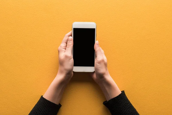 Vista ritagliata di donna che tiene smartphone con schermo vuoto su sfondo arancione — Foto stock