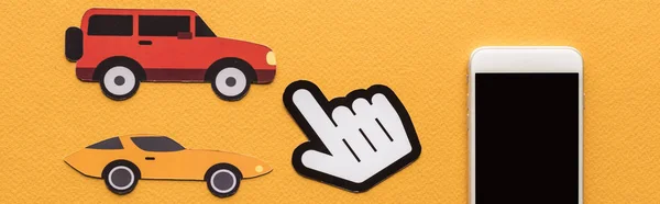 Draufsicht auf papiergeschnittene Autos, zeigende Hand und Smartphone auf orangefarbenem Hintergrund, Panoramaaufnahme — Stockfoto