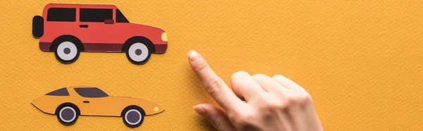 Cropped view of woman pointing with finger at paper cars on orange background, panoramic shot — Stock Photo