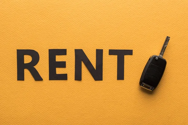 Top view of paper cut rent lettering and car key on orange background — Stock Photo
