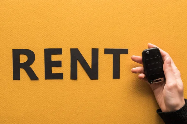 Cropped view of woman holding car key near paper cut rent lettering on orange background — Stock Photo