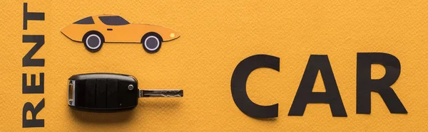 Vista superior de papel cortado aluguel de carro lettering e chave no fundo laranja, tiro panorâmico — Fotografia de Stock