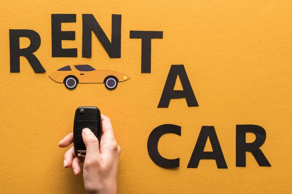 Cropped view of woman holding key near paper cut rent a car lettering on orange background — Stock Photo