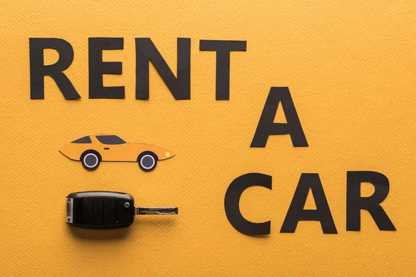 Vista superior de papel corte alquiler coche letras y clave sobre fondo naranja - foto de stock