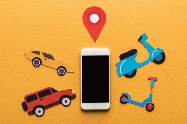 Draufsicht auf papiergeschnittene Fahrzeuge in der Nähe von Ortsmarke und Smartphone mit leerem Bildschirm auf orangefarbenem Hintergrund — Stockfoto
