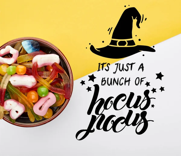 Top view of colorful gummy sweets in bowl on yellow and white background with it is just a bunch of hocus pocus illustration — Stock Photo