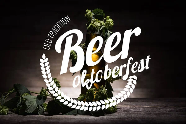 Cerveza fresca en botella con lúpulo verde en la superficie de madera en la oscuridad con la vieja tradición de cerveza Oktoberfest ilustración — Stock Photo