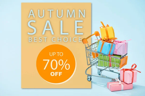 Festive wrapped presents in shopping cart on blue background with autumn sale, up to 70 percent off illustration — Stock Photo