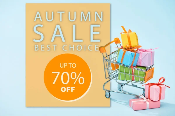 Regalos envueltos festivos en el carrito de la compra sobre fondo azul con la venta de otoño, hasta 70 por ciento de ilustración - foto de stock