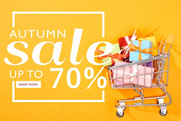 Top view of shopping cart with presents on bright orange background with autumn sale, up to 70 percent illustration — Stock Photo
