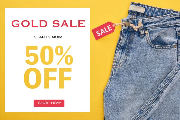 Top view of jeans with sale label on yellow background with gold sale 50 percent off illustration — Stock Photo