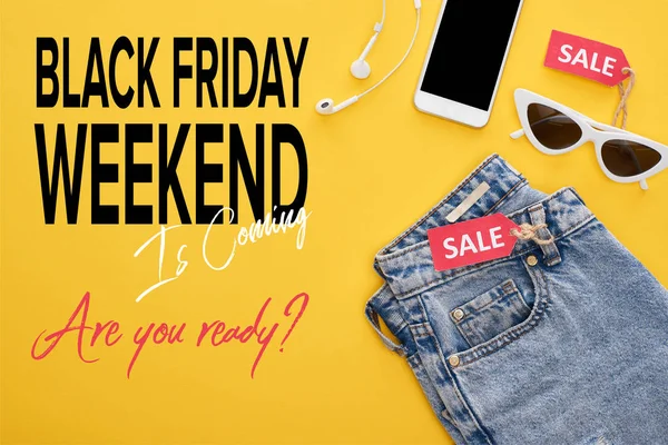 Верхний вид джинсы, очки и смартфон с наушниками с ярлыками продажи на желтом фоне с черной иллюстрацией пятницы выходные — стоковое фото