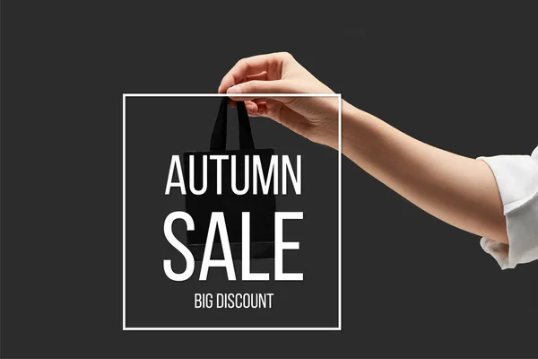 Vista recortada de la mujer sosteniendo pequeño bolso de compras negro en mano aislado en negro con ilustración de venta de otoño - foto de stock