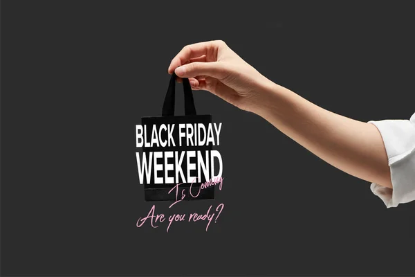 Vista recortada de la mujer sosteniendo pequeño bolso de compras negro en mano aislado en negro con ilustración de fin de semana de viernes negro - foto de stock