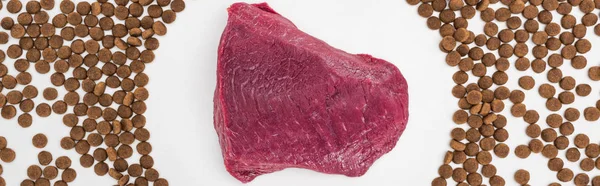 Draufsicht auf trockenes Tiernahrung verstreut um rohes Fleisch isoliert auf weißer, panoramischer Aufnahme — Stockfoto