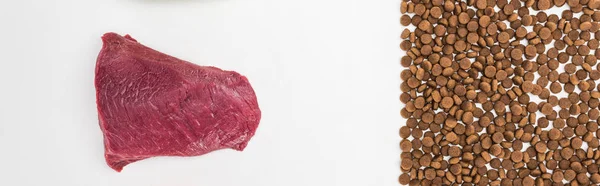 Draufsicht auf Trockenfutter in der Nähe von rohem Fleisch vereinzelt auf weißem, panoramischem Foto — Stockfoto