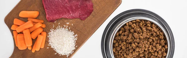 Vista dall'alto di cibo secco per animali domestici e carne cruda, riso, carota su tagliere di legno isolato su bianco, colpo panoramico — Foto stock