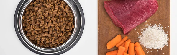 Vista superior de alimentos secos para animais de estimação e carne crua, arroz, cenoura em tábua de corte de madeira isolada em branco, tiro panorâmico — Fotografia de Stock