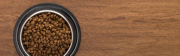 Vista superior de comida seca para mascotas en un tazón de plata sobre una mesa de madera, plano panorámico - foto de stock