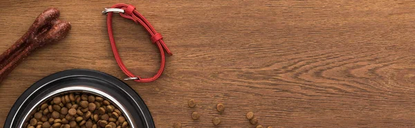 Top view of dry pet food in silver bowl near bones, collar on wooden table, panoramic shot — Stock Photo