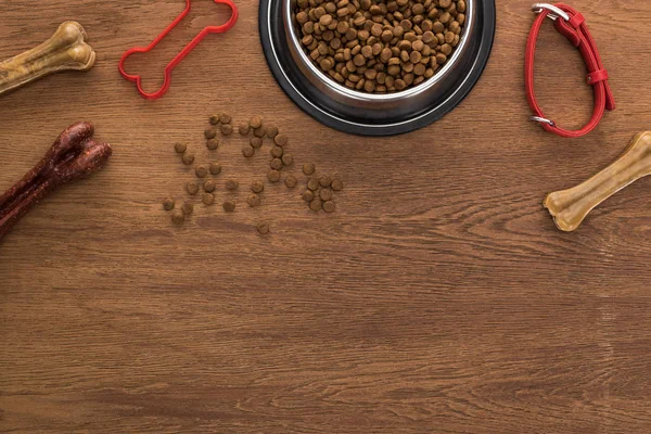 Vista dall'alto del cibo secco per animali in una ciotola d'argento vicino alle ossa, al colletto e al giocattolo per animali su un tavolo di legno — Foto stock