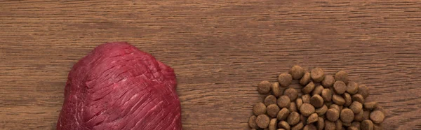 Top view of dry pet food near raw meat on wooden table, panoramic shot — Stock Photo