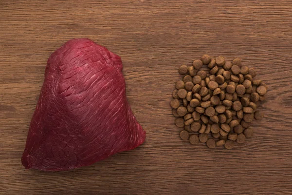 Vue du dessus des aliments secs pour animaux de compagnie près de la viande crue sur une table en bois — Photo de stock