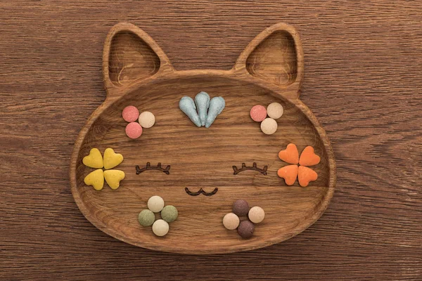 Draufsicht auf Katzen-Trockenfutter und Vitamine in niedlicher Katzenform Teller auf Holztisch — Stockfoto