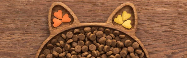 Vista superior de alimentos para animais de estimação secos felinos e vitaminas na placa de forma de gato na mesa de madeira, tiro panorâmico — Fotografia de Stock