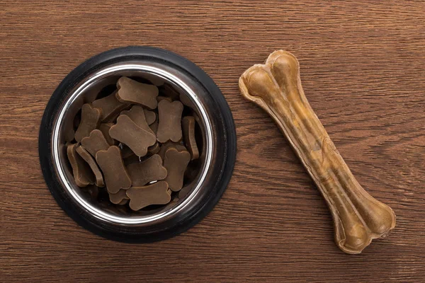 Top view of dry pet food in silver bowl near bone on wooden table — Stock Photo