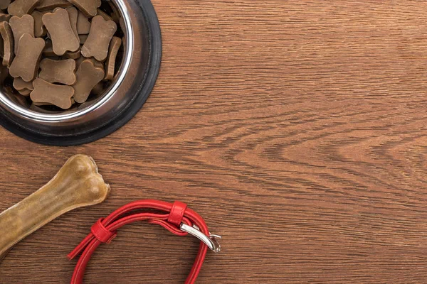 Vista superior de comida seca para mascotas en tazón de plata cerca de hueso, cuello en mesa de madera - foto de stock