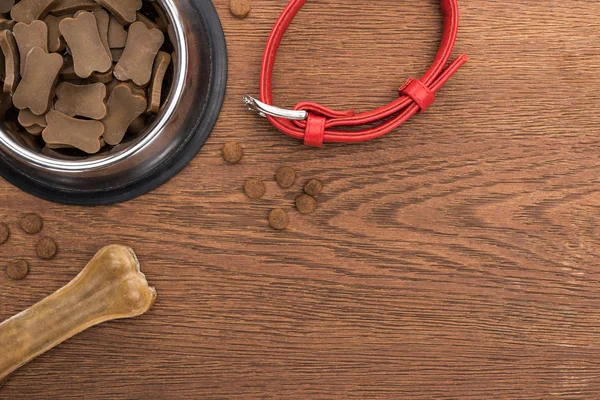 Vista dall'alto del cibo secco per animali domestici in una ciotola d'argento vicino all'osso, colletto su un tavolo di legno — Foto stock