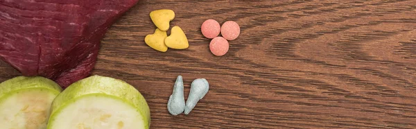 Top view of raw meet, zucchini near pet vitamins on wooden table, panoramic shot — Stock Photo