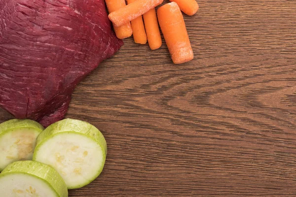 Top view of raw meet, zucchini and carrot on wooden table — Stock Photo