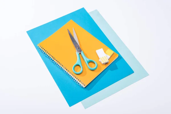 Vista ad angolo alto di forbici, notebook, gomme e carta isolata su bianco — Foto stock