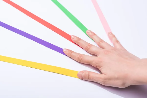 Vista recortada de la mujer tocando tiras de papel de colores sobre fondo blanco - foto de stock