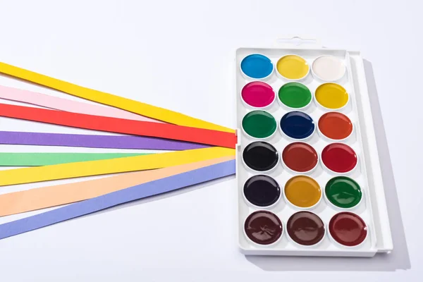 Vista de alto ângulo de aquarela e tiras de papel brilhante no fundo branco — Fotografia de Stock